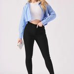 A blonde woman posing in high rise black jeggings for women paired with a blue shirt and white crop top.