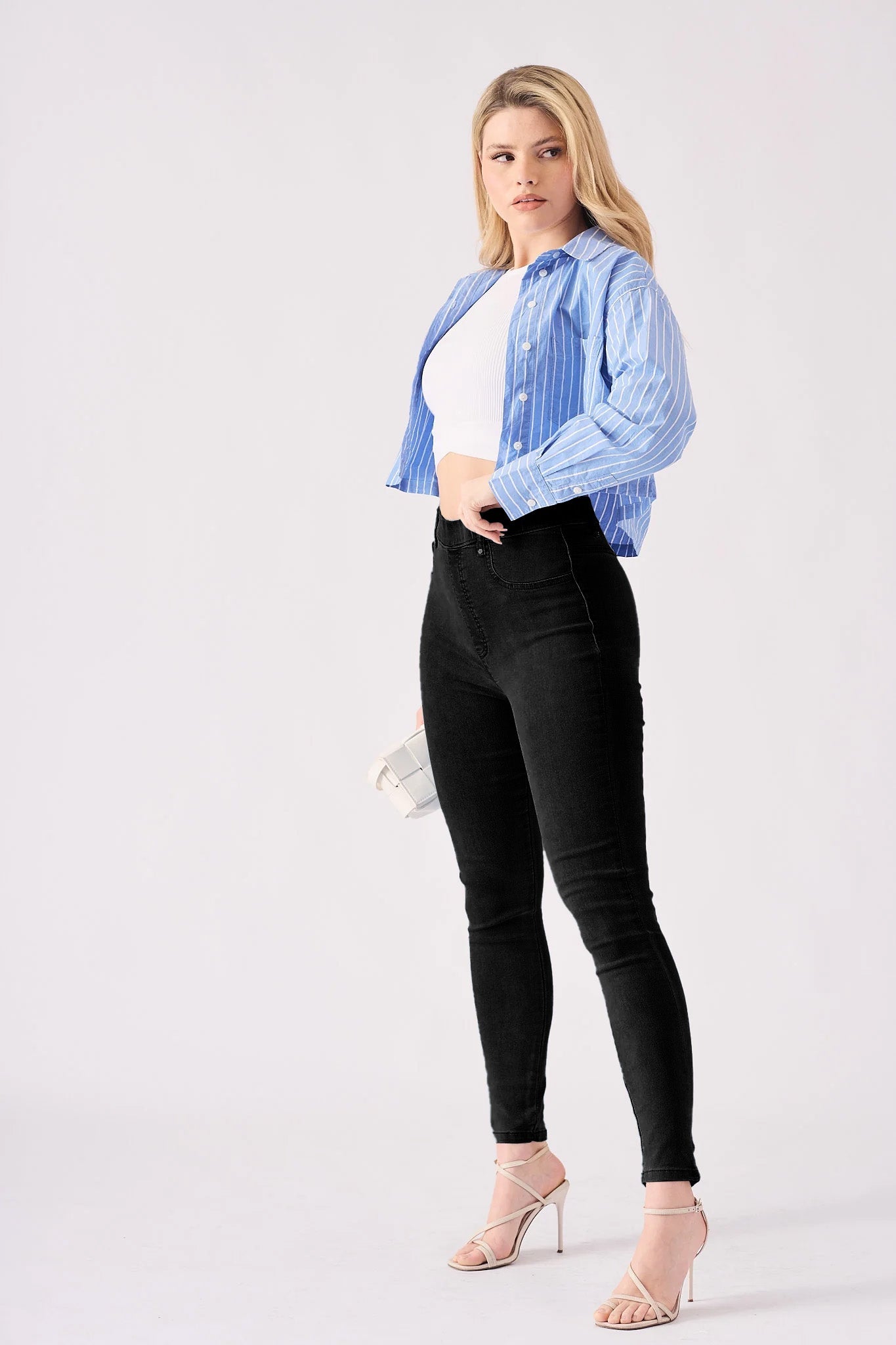 A side on shot of a model wearing high rise black jeggings for women with heels.