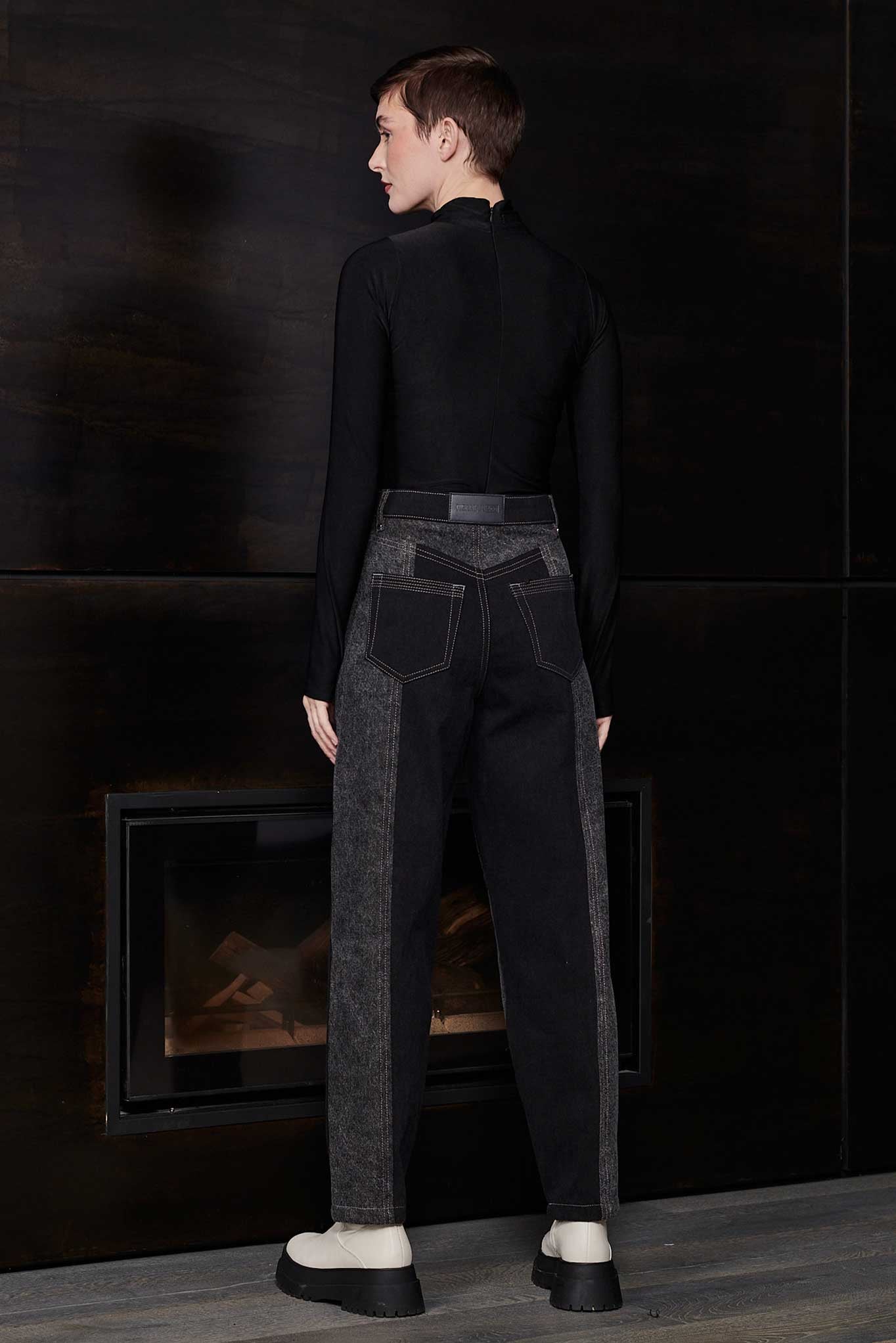 Back view of model wearing Jmojo black acid wash tapered jeans with vegan leather branding patch