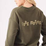 Rear view of a woman wearing a khaki crew neck jumper showing the bold core motive branding