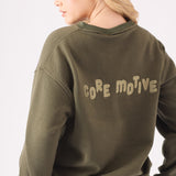 Rear view of a woman wearing a khaki crew neck jumper showing the bold core motive branding
