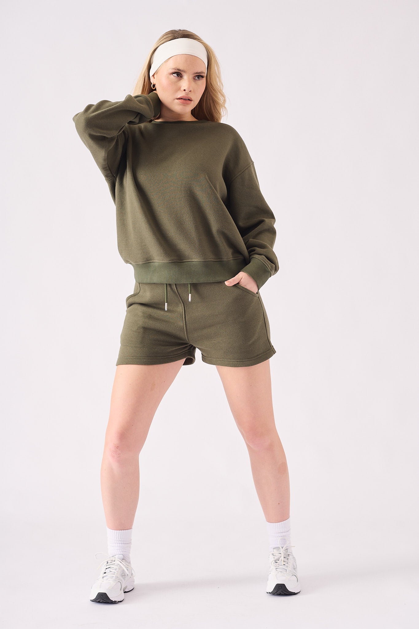 A front view of a woman wearing a khaki crew neck jumper with matching shorts and a headband