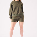 A woman posing in a khaki crew neck jumper with a white headband for a casual look