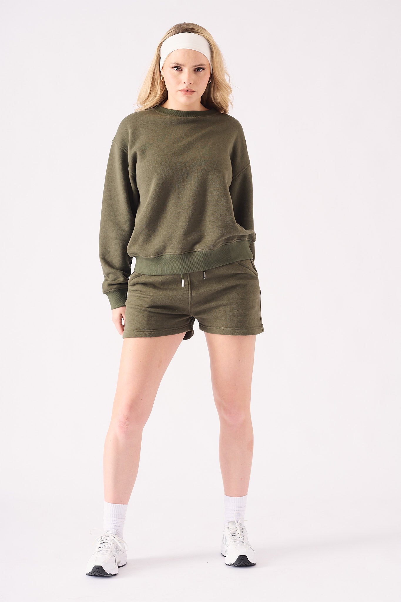 A woman posing in a khaki crew neck jumper with a white headband for a casual look
