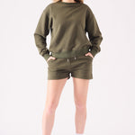 Full front view of a model styling a khaki crew neck jumper and shorts set with white trainers