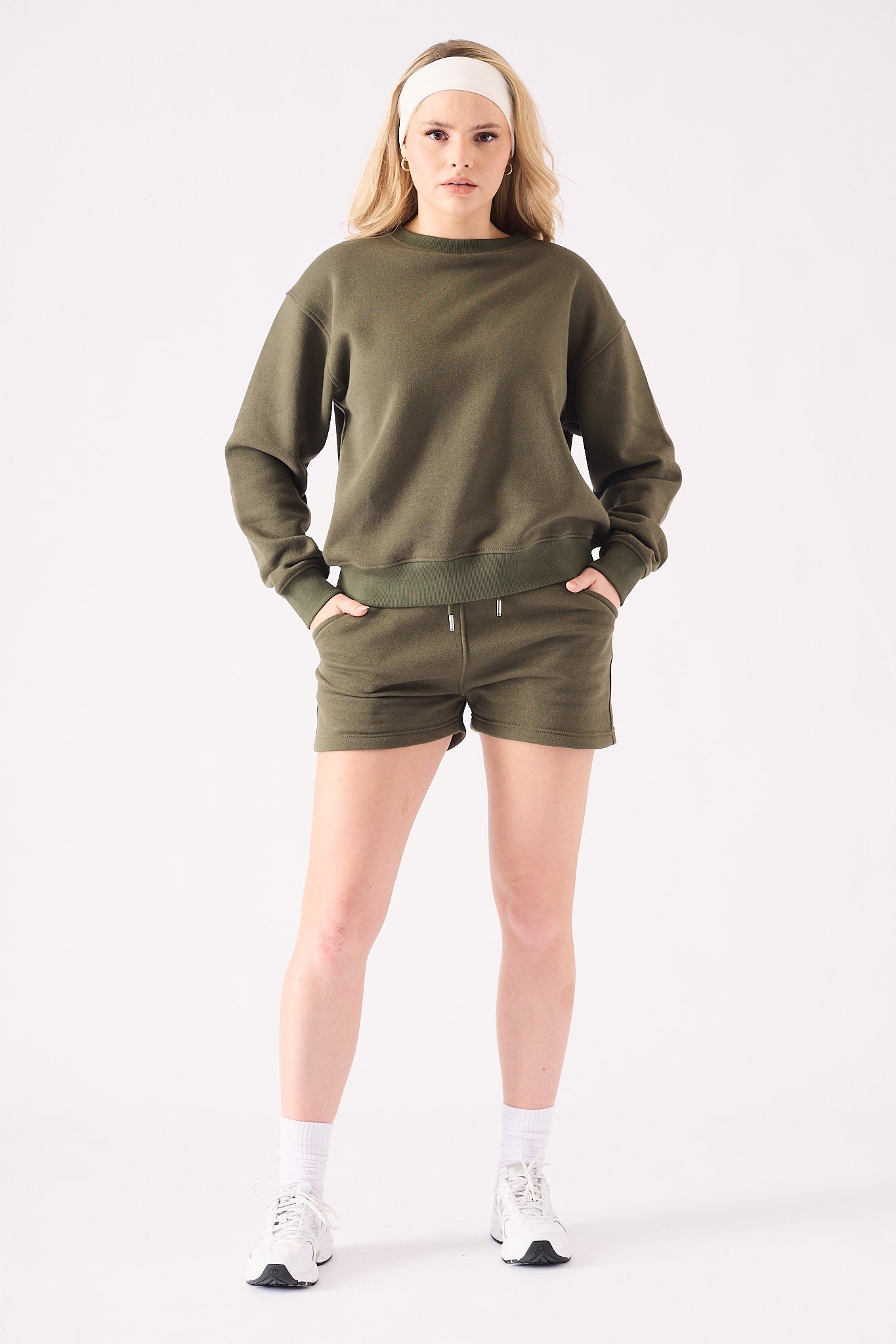 Full front view of a model styling a khaki crew neck jumper and shorts set with white trainers