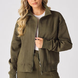 A blonde woman wearing a khaki zip up sweatshirt looking at the camera