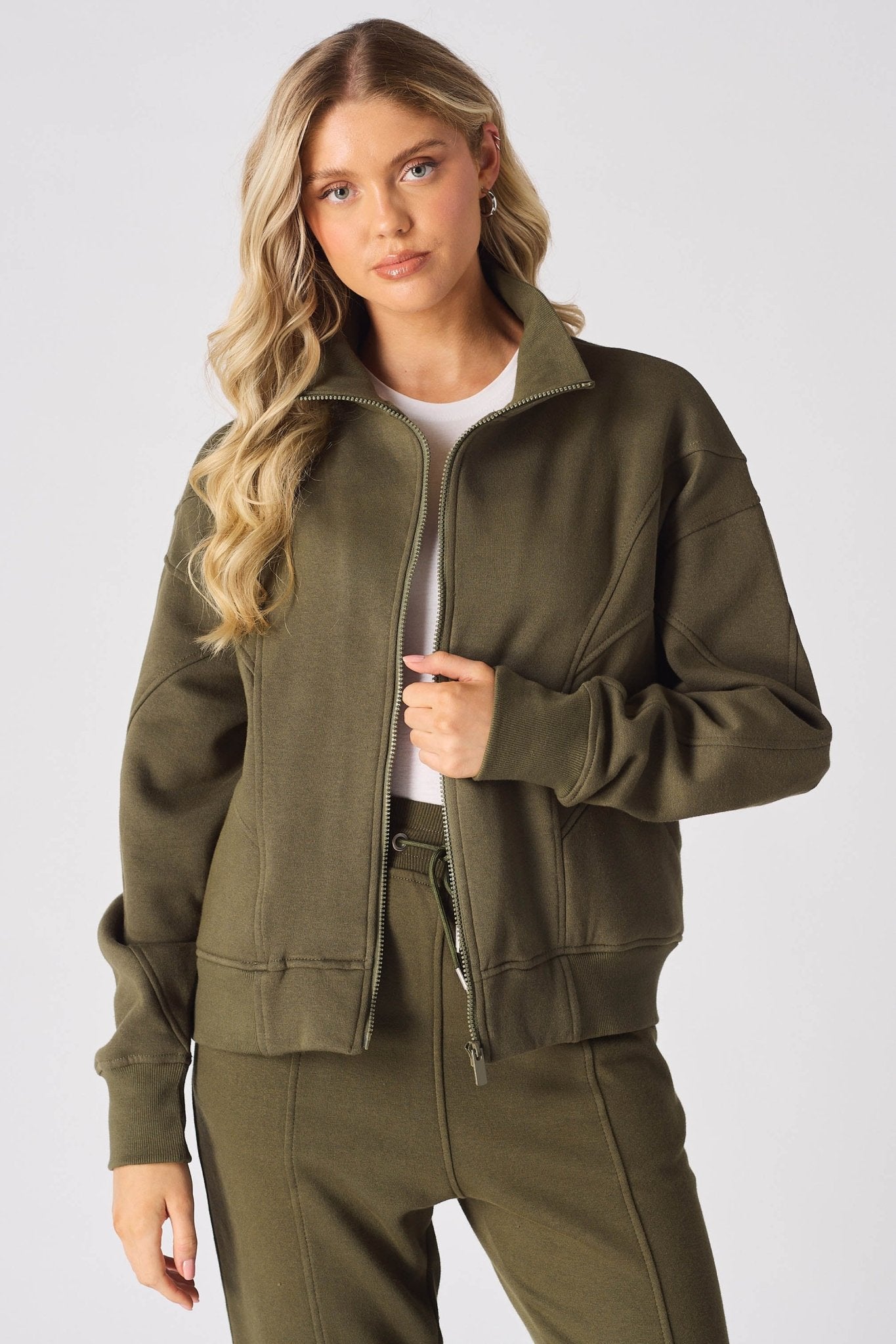 A blonde woman wearing a khaki zip up sweatshirt looking at the camera