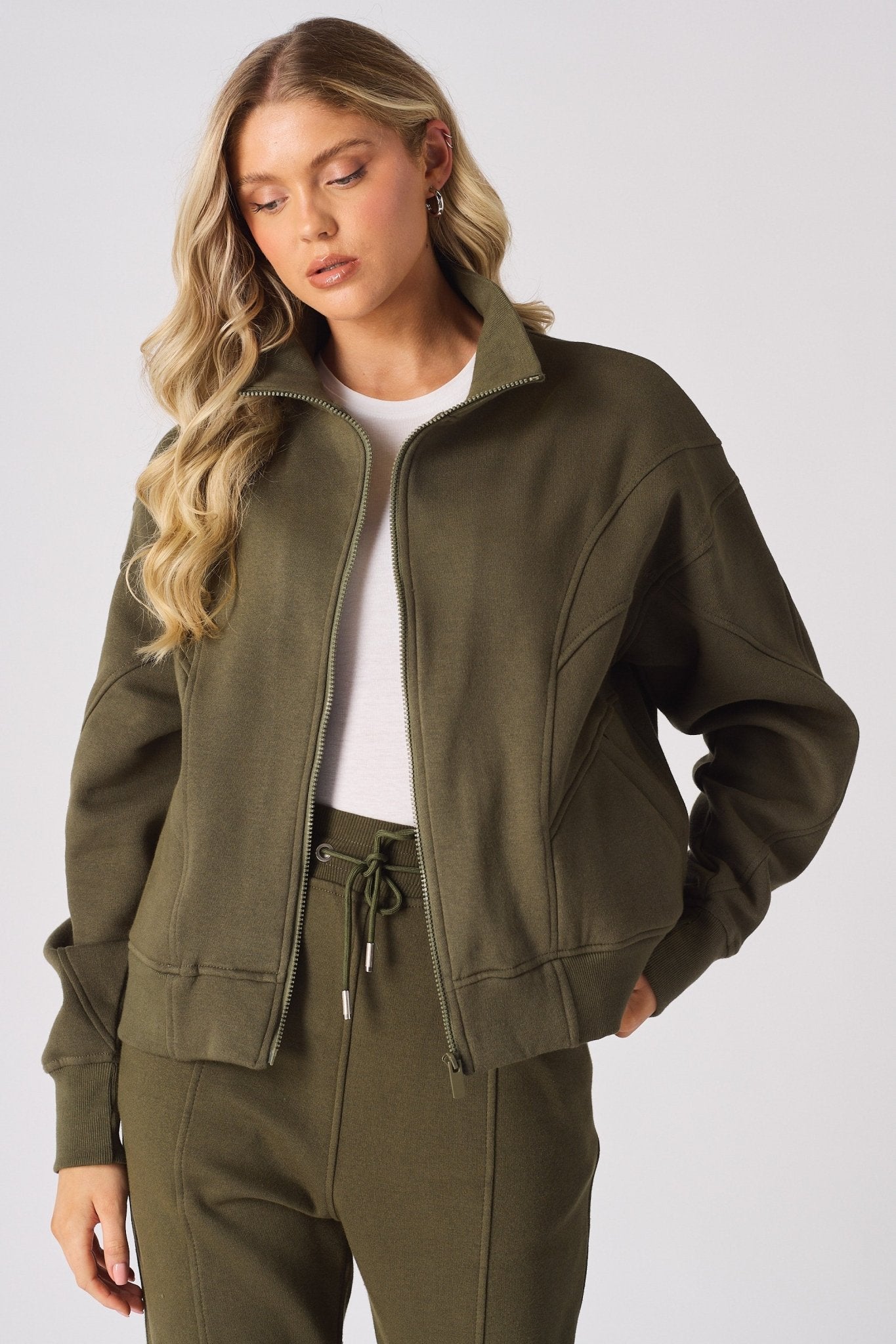 A model posing in a khaki zip up sweatshirt with a white t shirt underneath