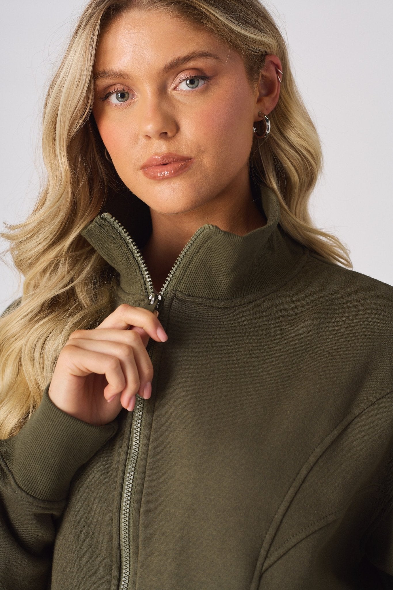 Close up of a hand adjusting the zip on a khaki funnel neck sweatshirt