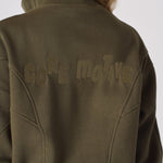 Detailed shot of the tonal embroidered branding on the back of a khaki sweatshirt
