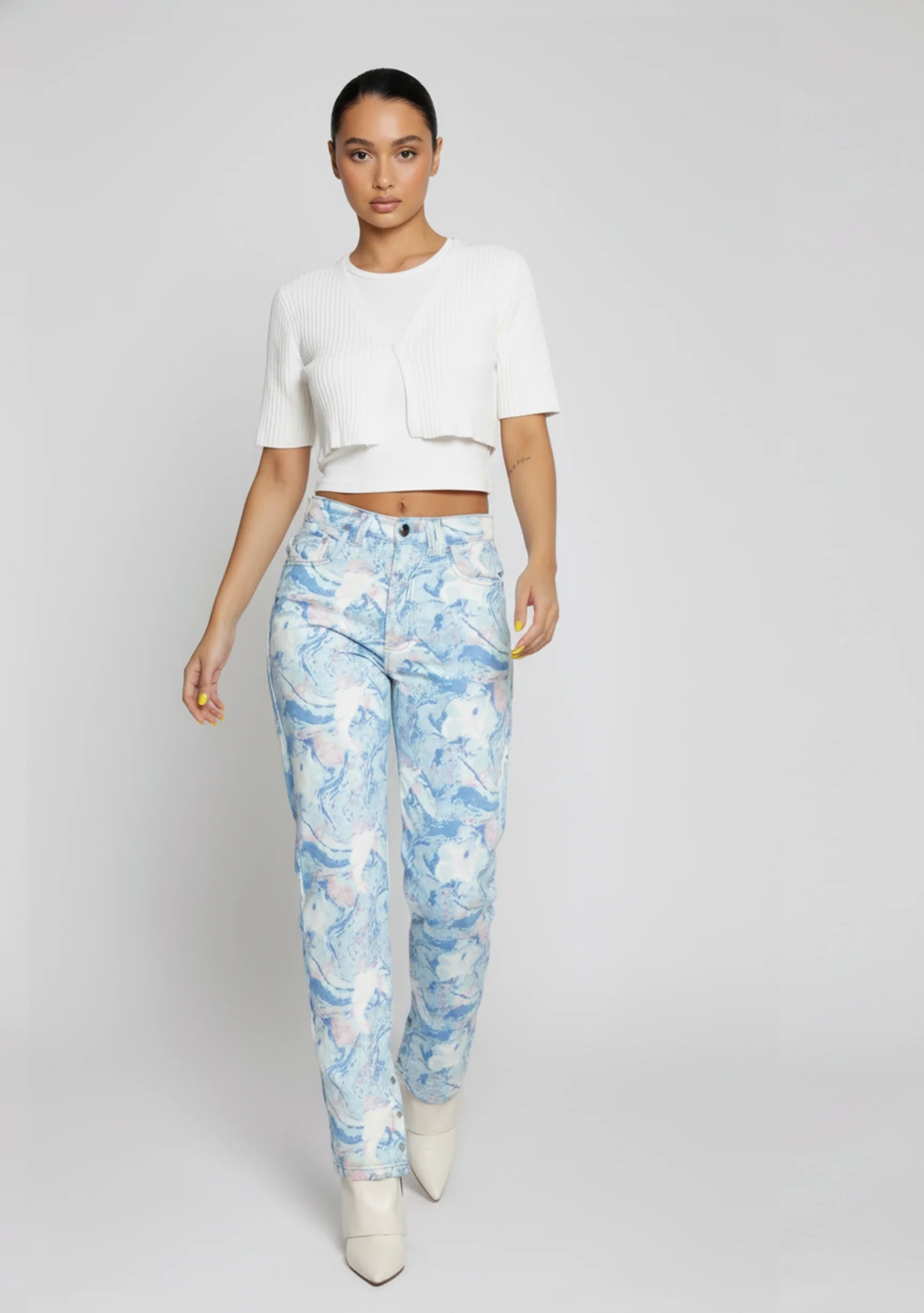 Close up of the front waist and button closure on high-rise light blue acid marble jeans.