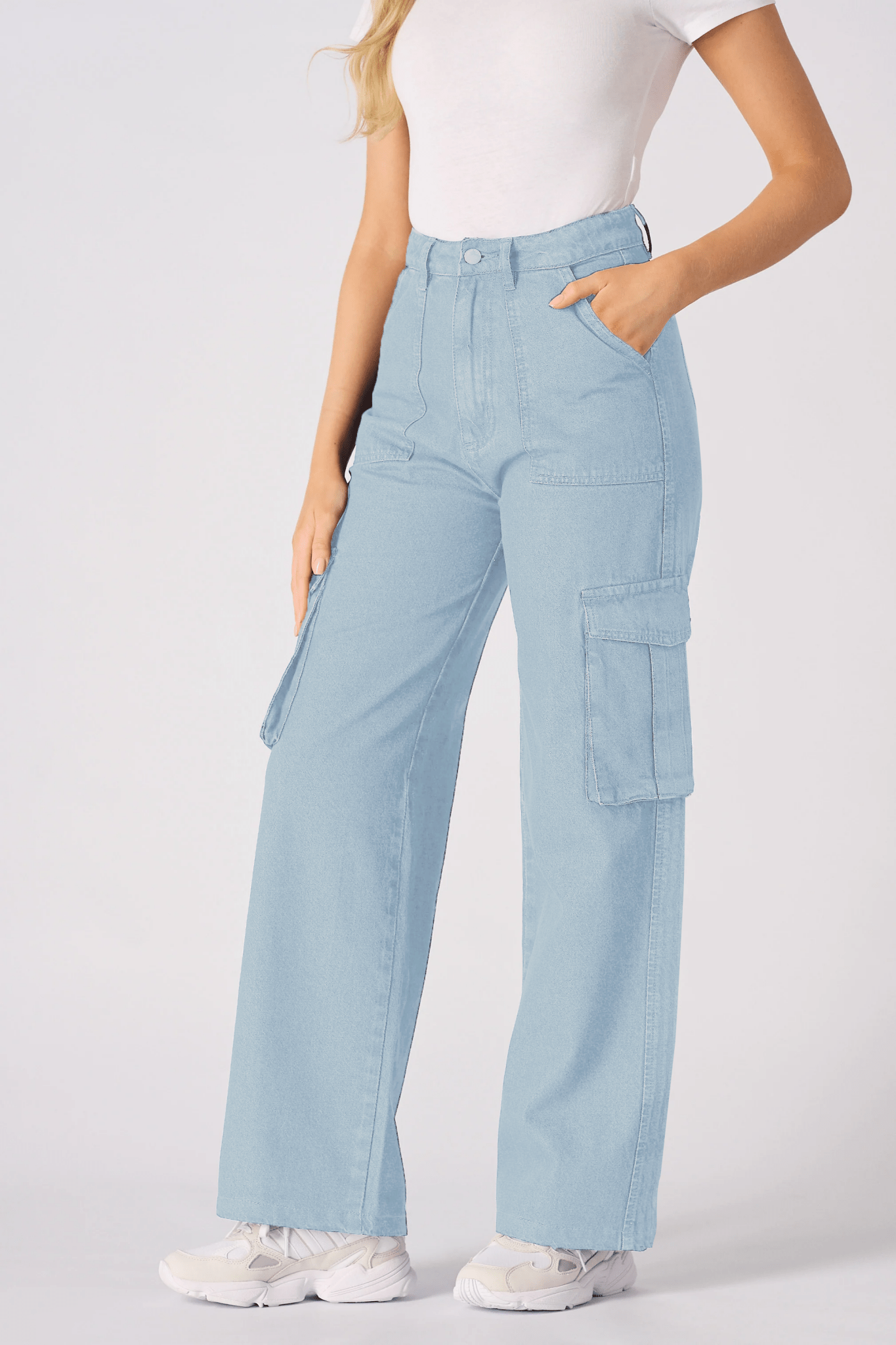 A full length shot of a model wearing light blue cargo jeans for women and white trainers.