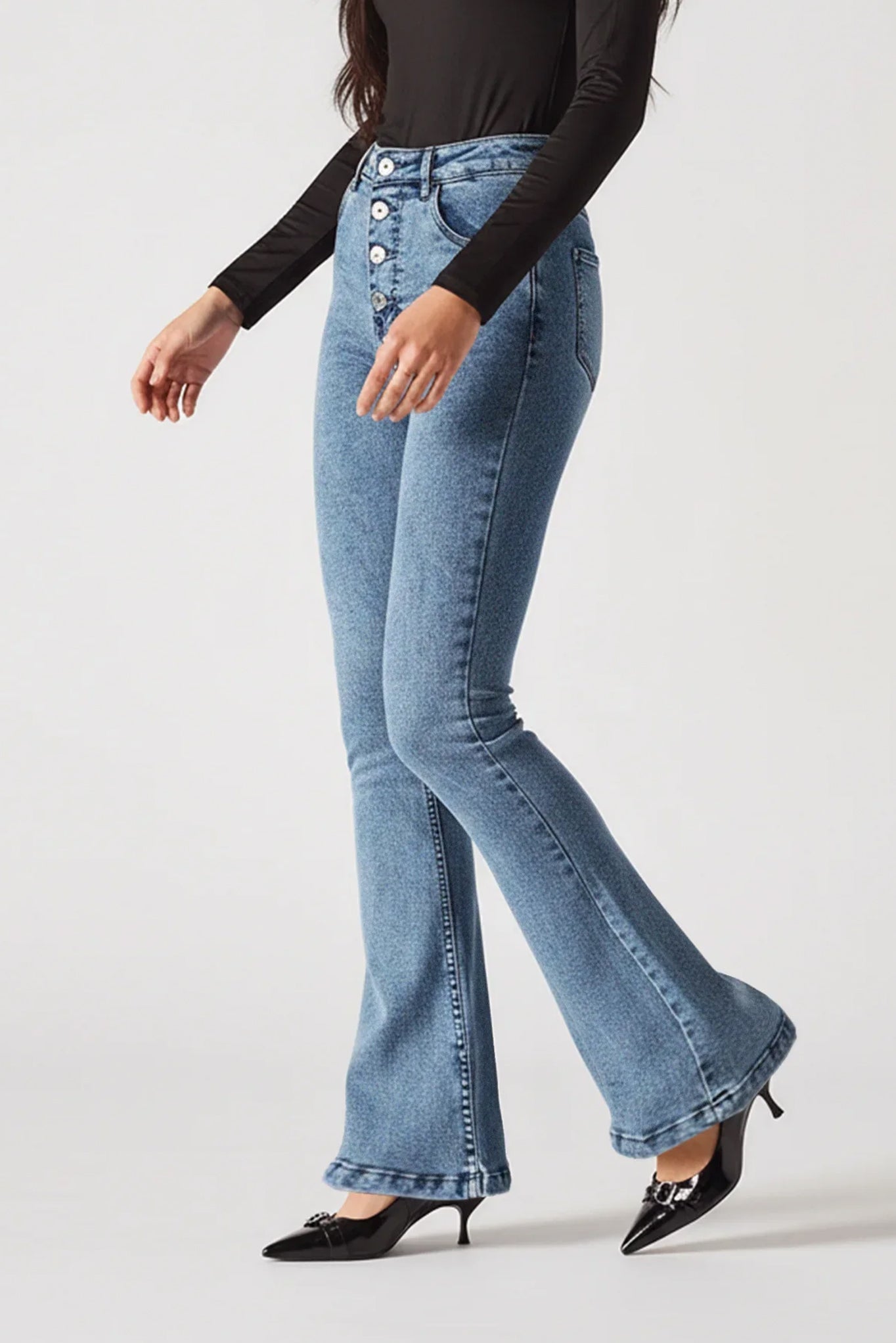 Person wearing light blue flared jeans and black top on a white background