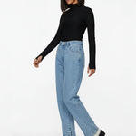 Side profile of a model walking in light blue straight leg jeans with snap button hem and front stud details.