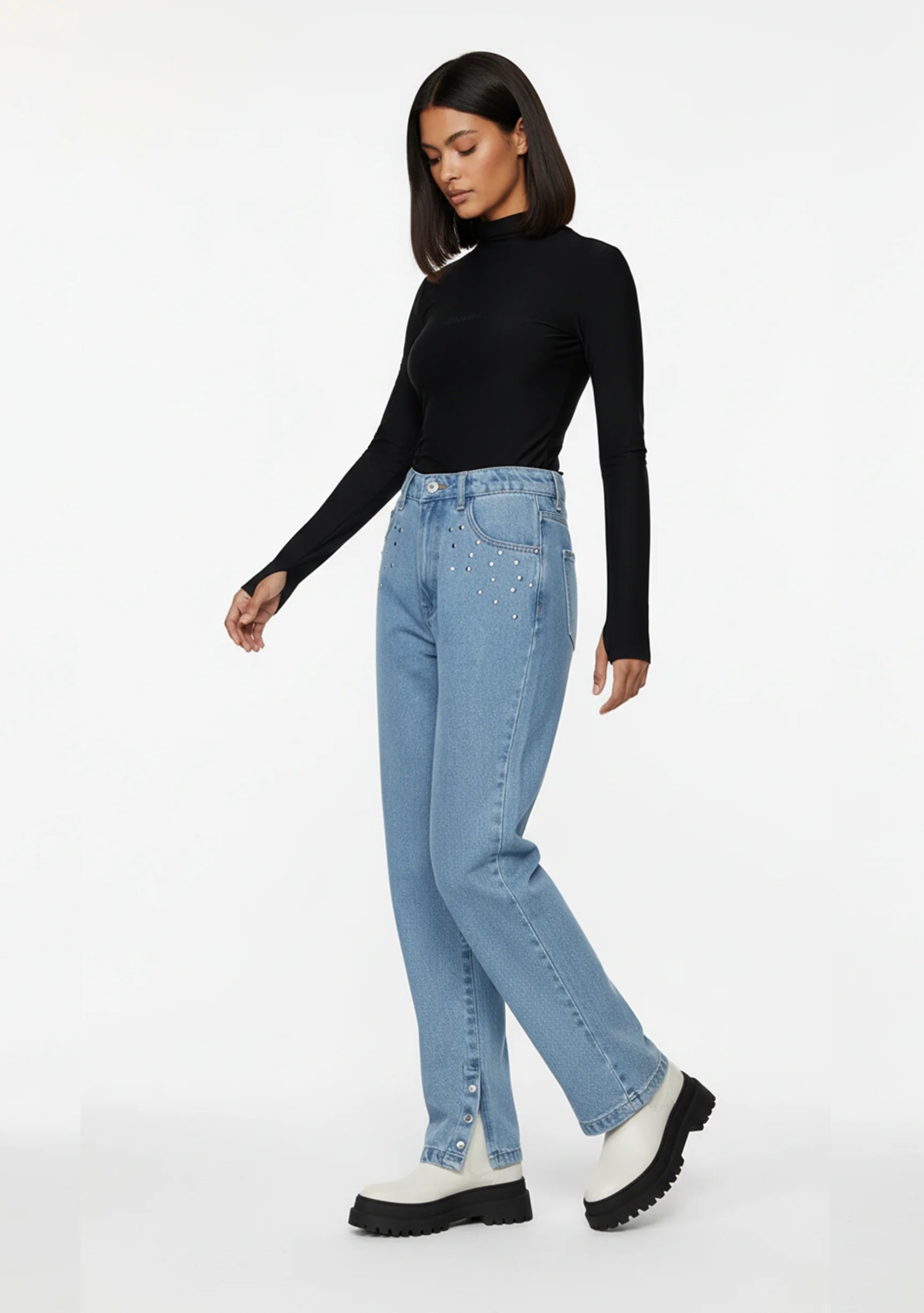 Side profile of a model walking in light blue straight leg jeans with snap button hem and front stud details.