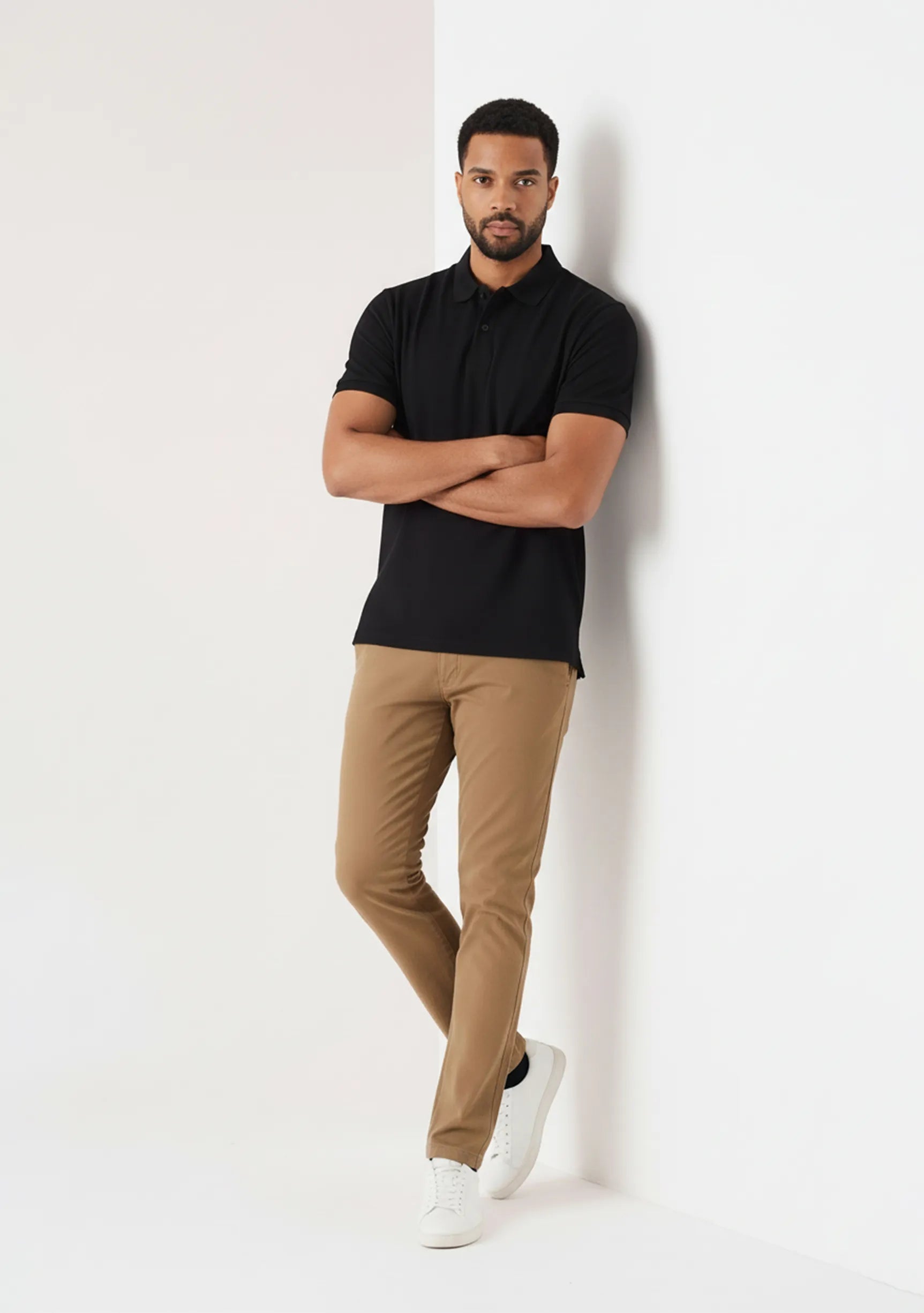 Model leaning against wall in men's light brown chinos