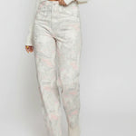 Person wearing light-colored floral jeans and a white top on a plain background
