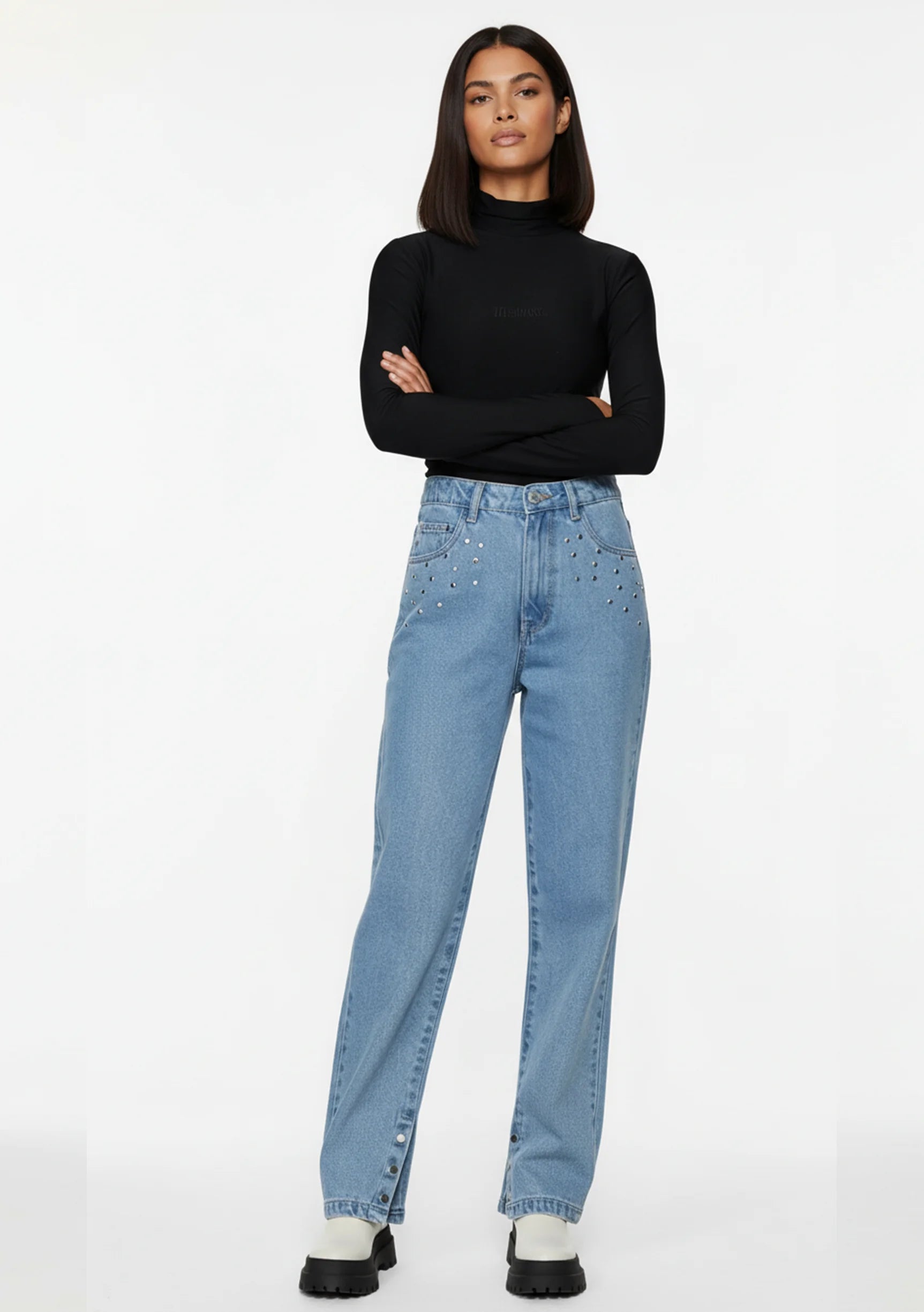 Model standing with arms crossed showcasing light denim straight leg pants featuring silver pocket studs.