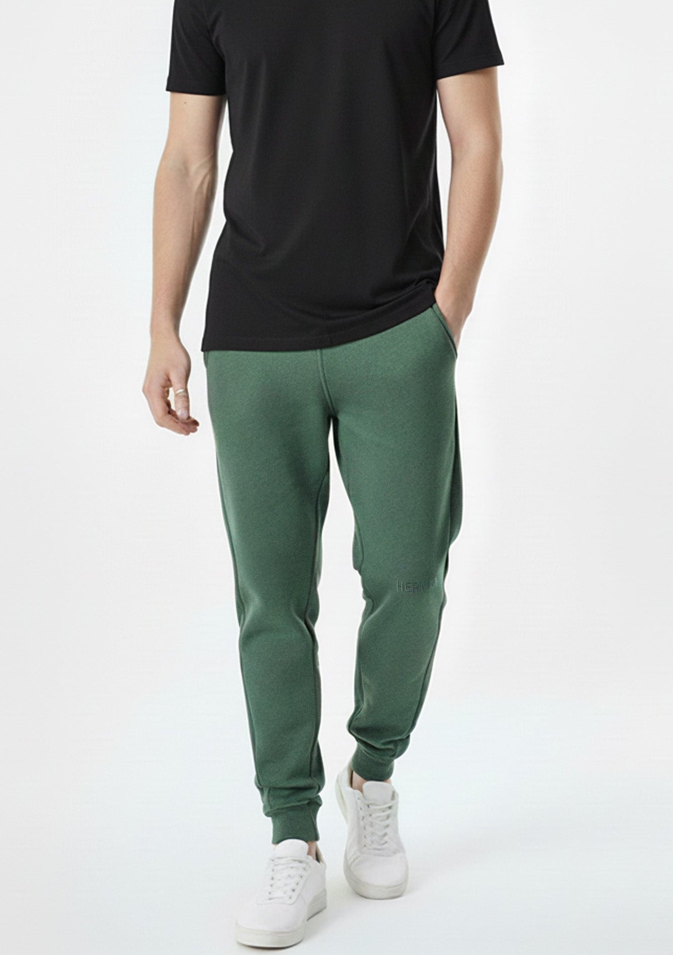 front view of man wearing dark green tapered joggers with white trainers