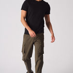 A man wearing slim fit green cotton cargo pants with a black t-shirt and trainers.
