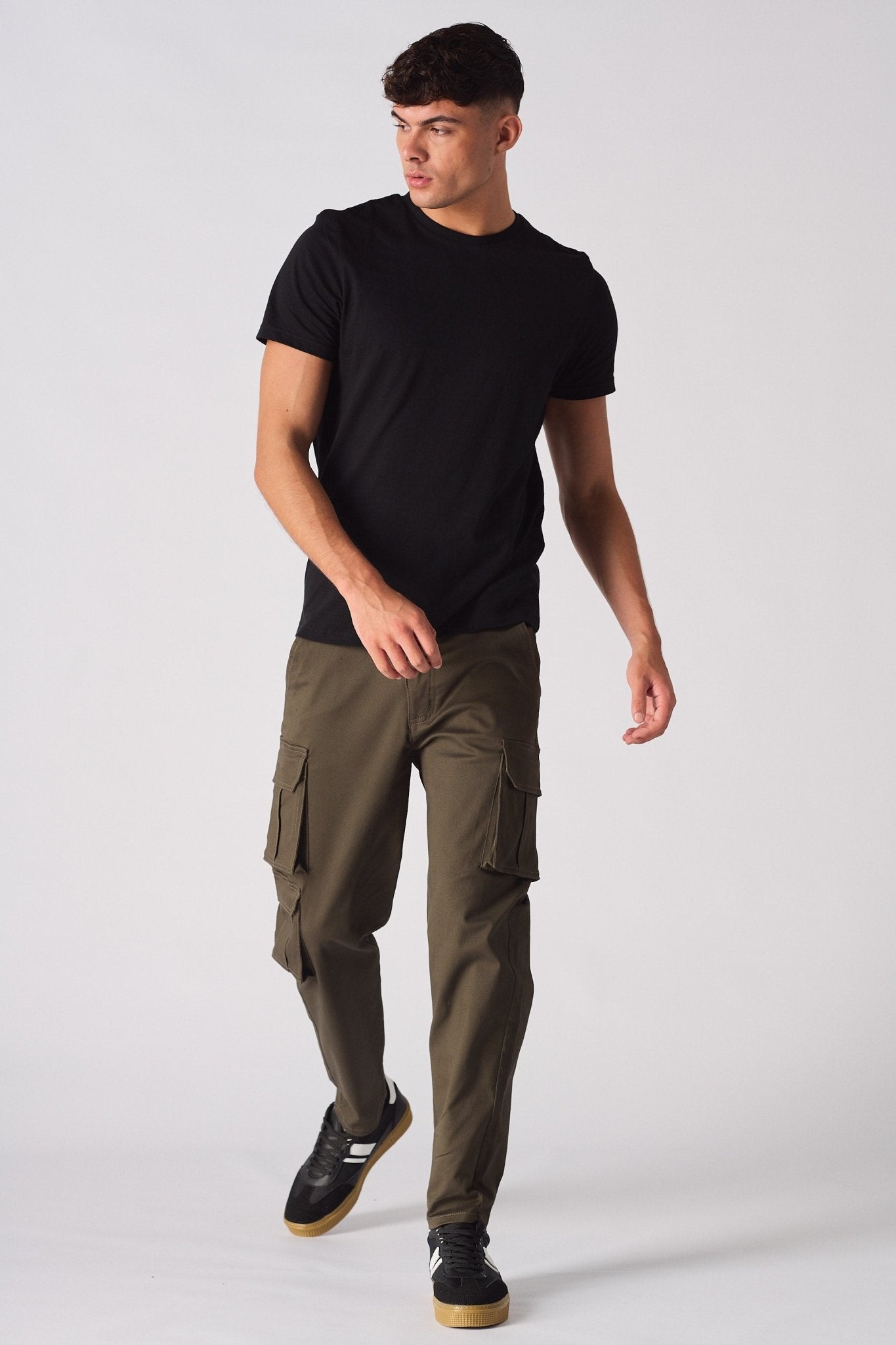 A man wearing slim fit green cotton cargo pants with a black t-shirt and trainers.