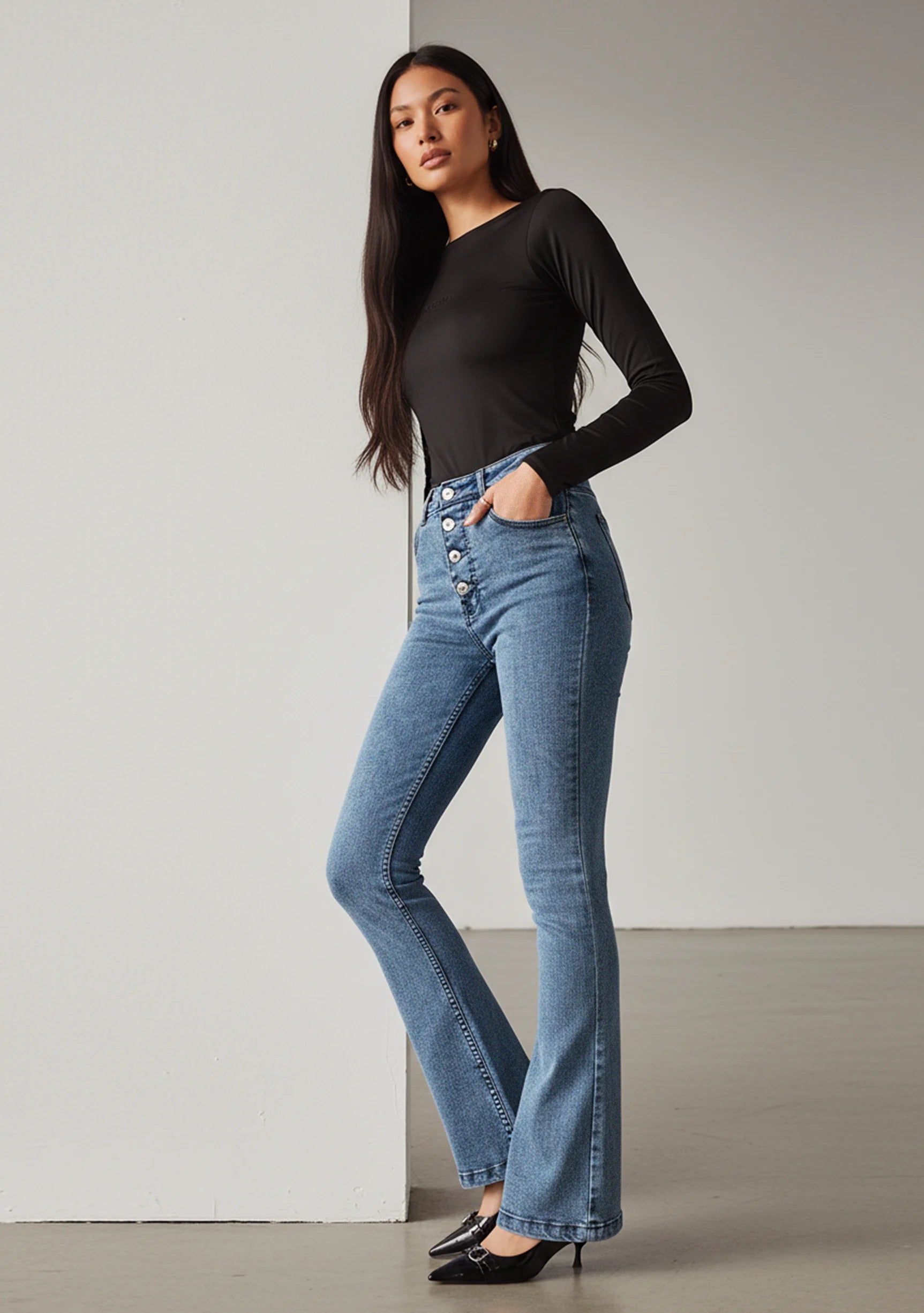 Model with arms crossed wearing high-waisted mid blue bootcut jeans