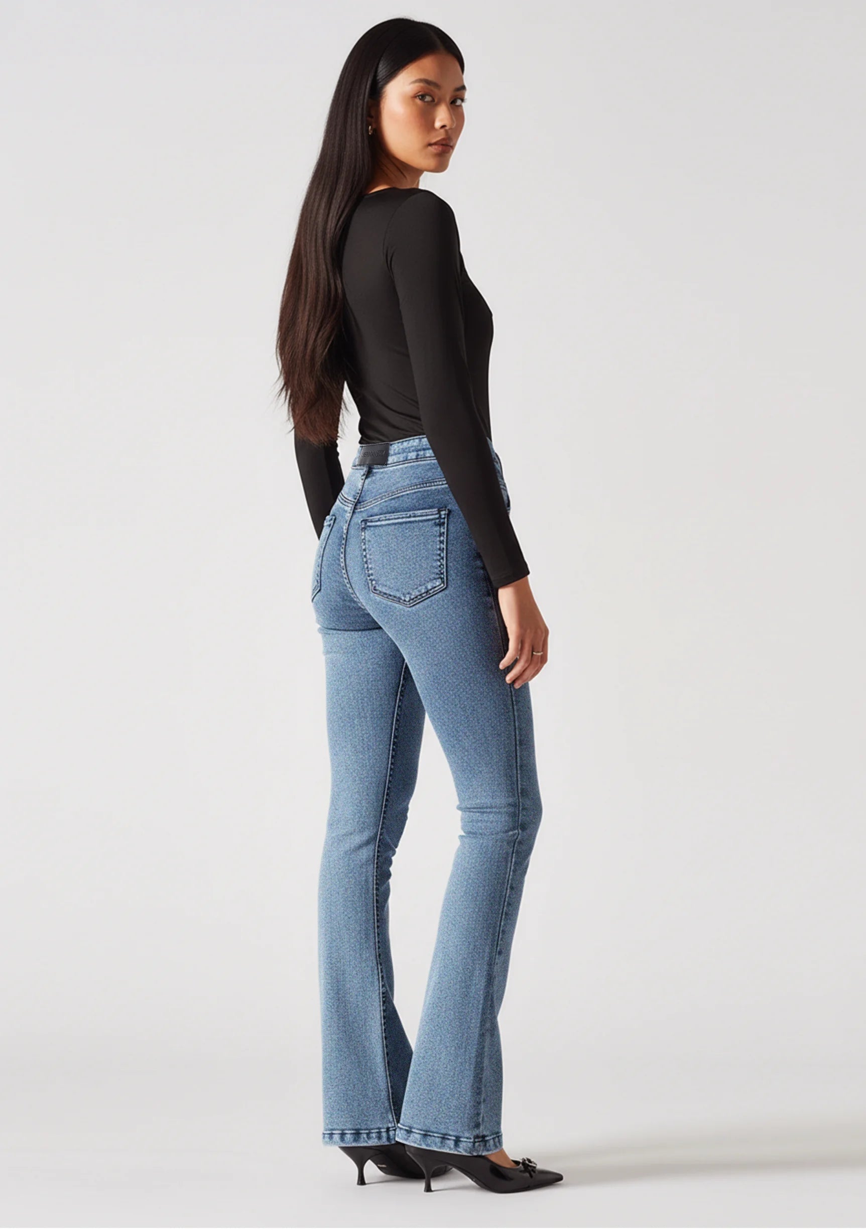 Full back view of model wearing form-fitting mid blue bootcut jeans