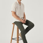 Model sitting on a wooden stool wearing comfortable and stretchable olive chinos mens.