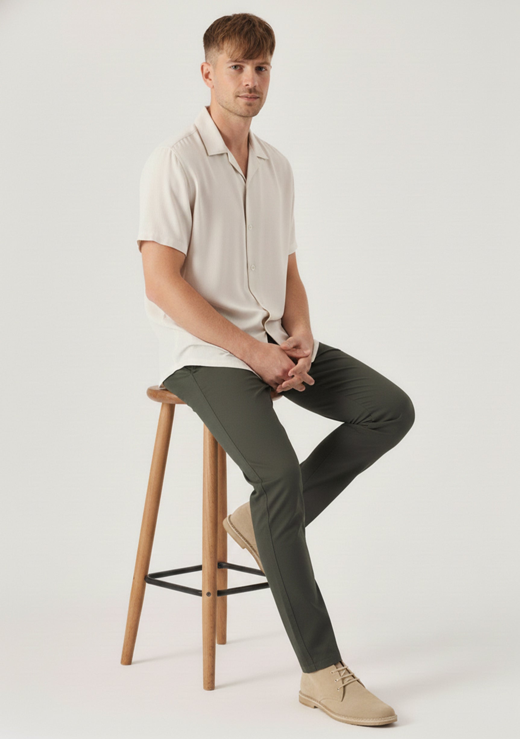 Model sitting on a wooden stool wearing comfortable and stretchable olive chinos mens.