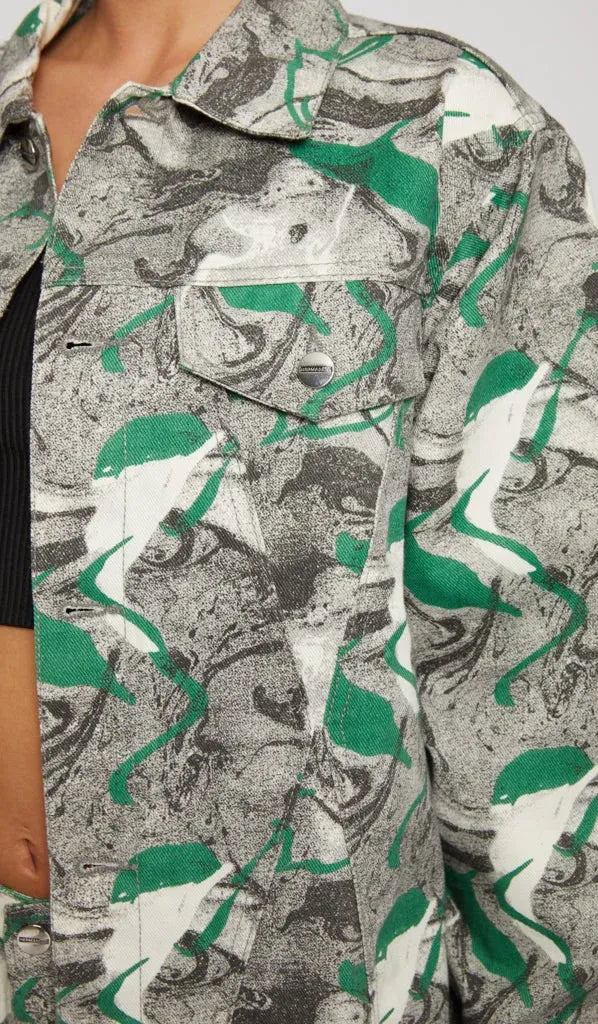 Close up of psychedelic print denim jacket chest pocket with silver button - showcasing green-grey-white abstract swirl fabric texture and collar detail