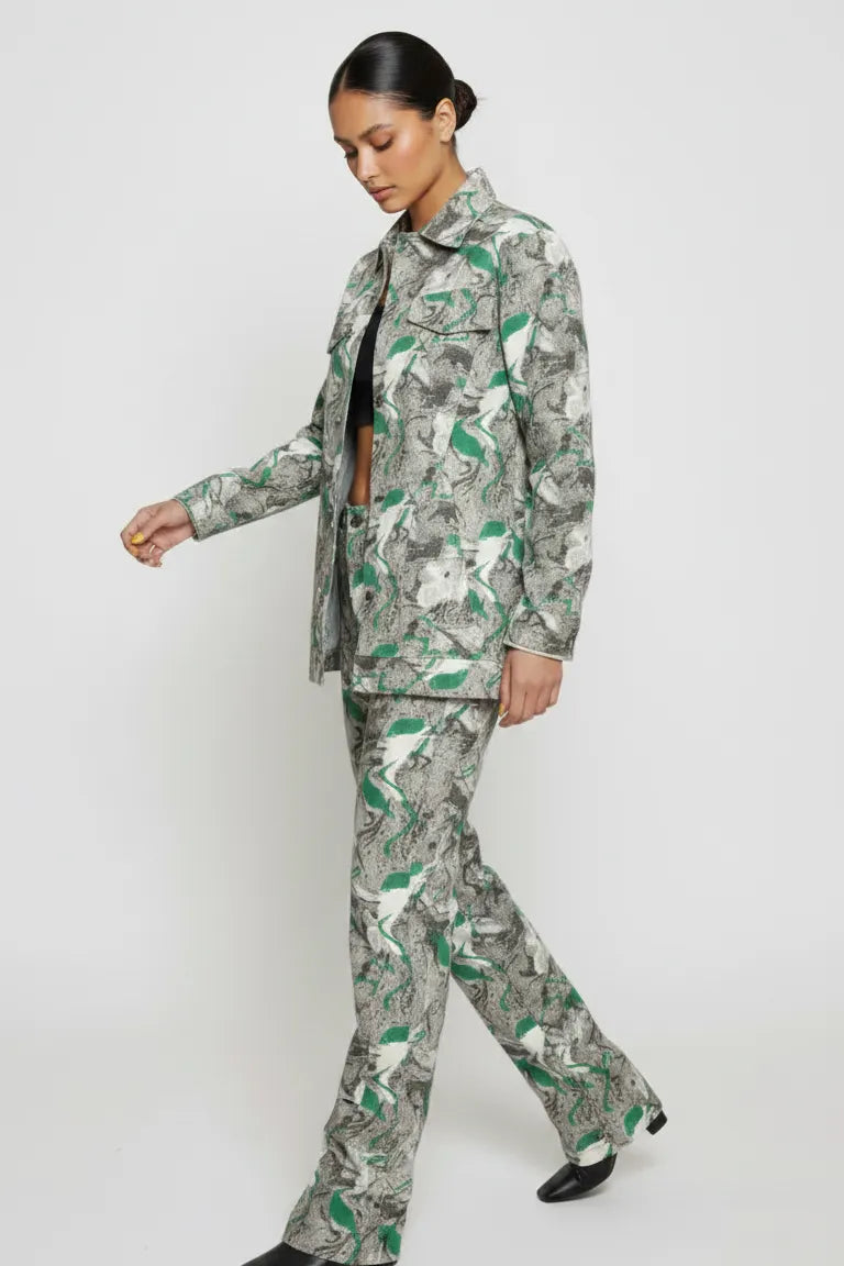 Side walking pose of psychedelic print denim jacket in motion - women’s green-grey abstract swirl patterned set with flared hem pants