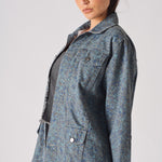 Close up front of speckle print denim jacket showing chest pockets, silver buttons, and mottled blue-grey pattern over black ribbed top