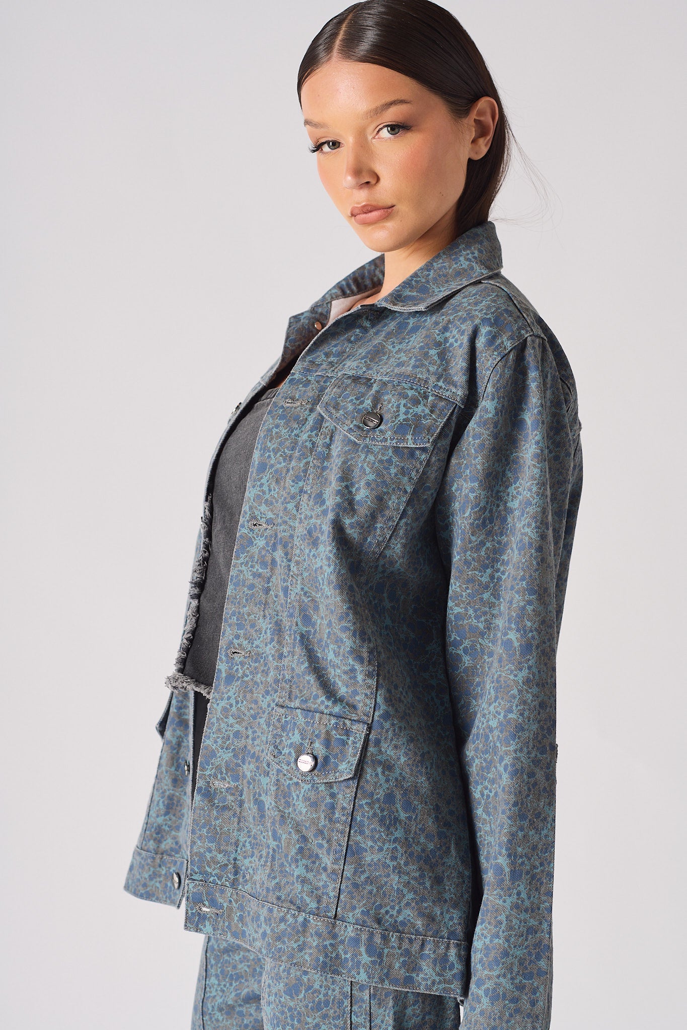 Close up front of speckle print denim jacket showing chest pockets, silver buttons, and mottled blue-grey pattern over black ribbed top