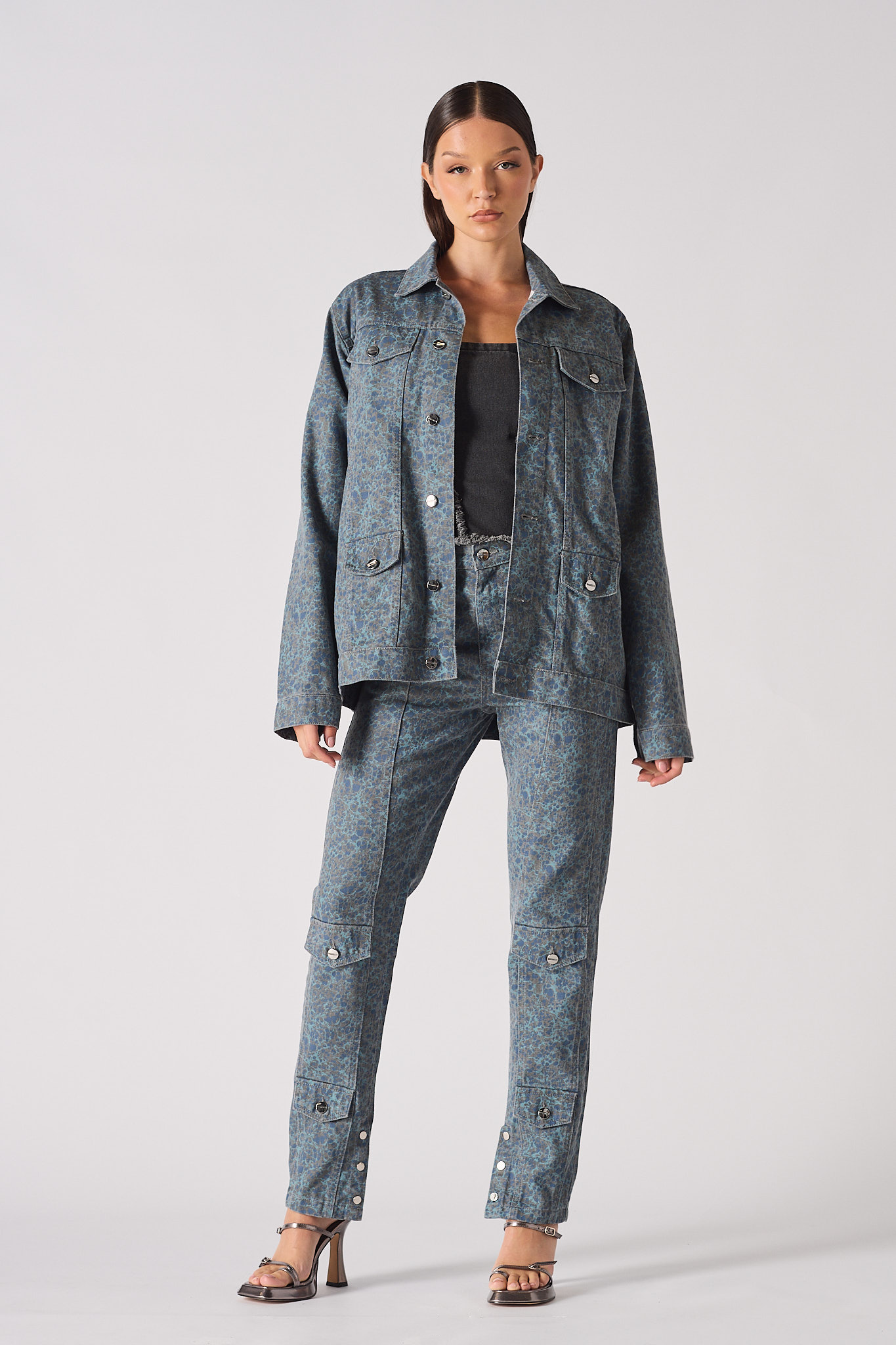 Front pose of speckle print denim jacket worn open with hands in pockets - women’s oversized acid wash set with chain belt and split-hem cargo pants
