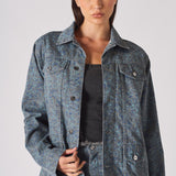 Mid-torso close up of speckle print denim jacket worn open over distressed corset top - showing layered texture and button placket detail
