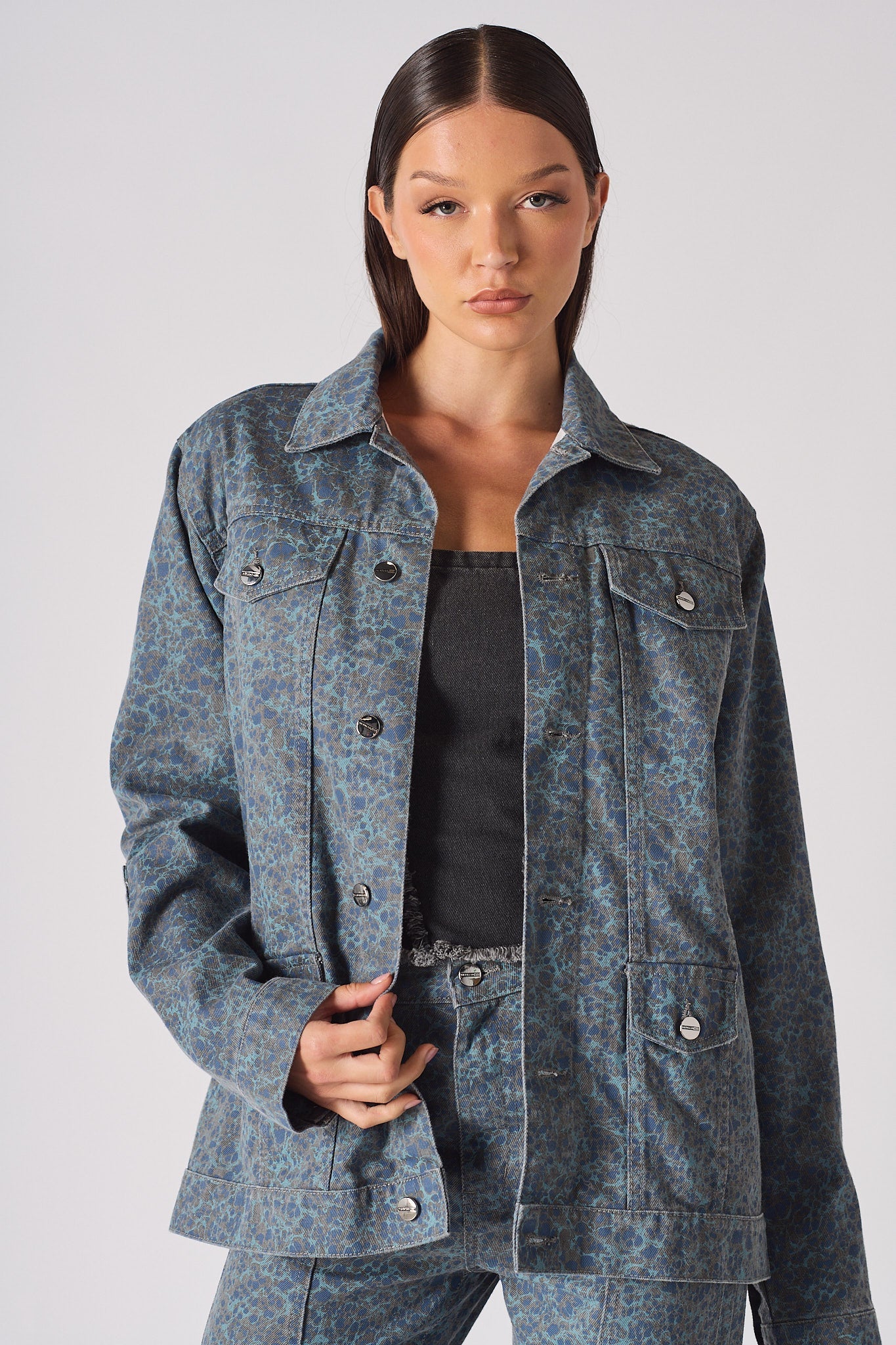 Mid-torso close up of speckle print denim jacket worn open over distressed corset top - showing layered texture and button placket detail