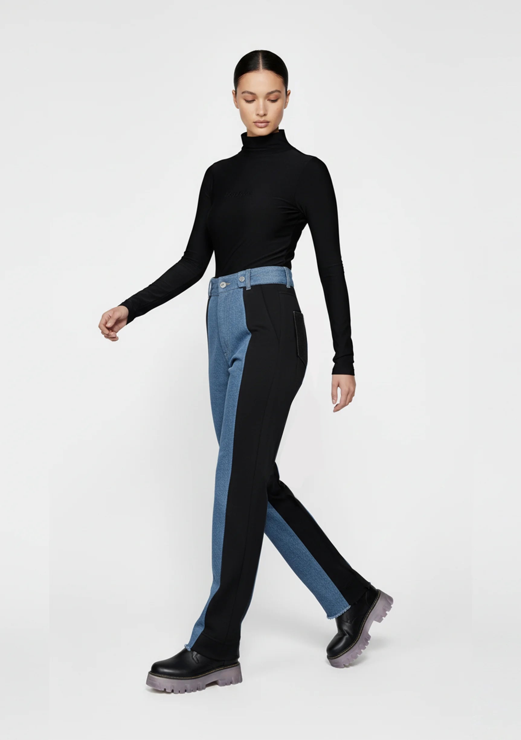 Studio shot of a model with folded arms showcasing spliced color high-rise jeans.