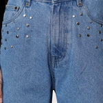 Close up of the high waist and silver studded embellishments around the front pockets on light wash denim.