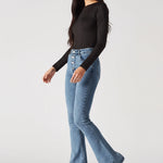 Front view of styled mid blue high-waisted bootcut jeans paired with a black top