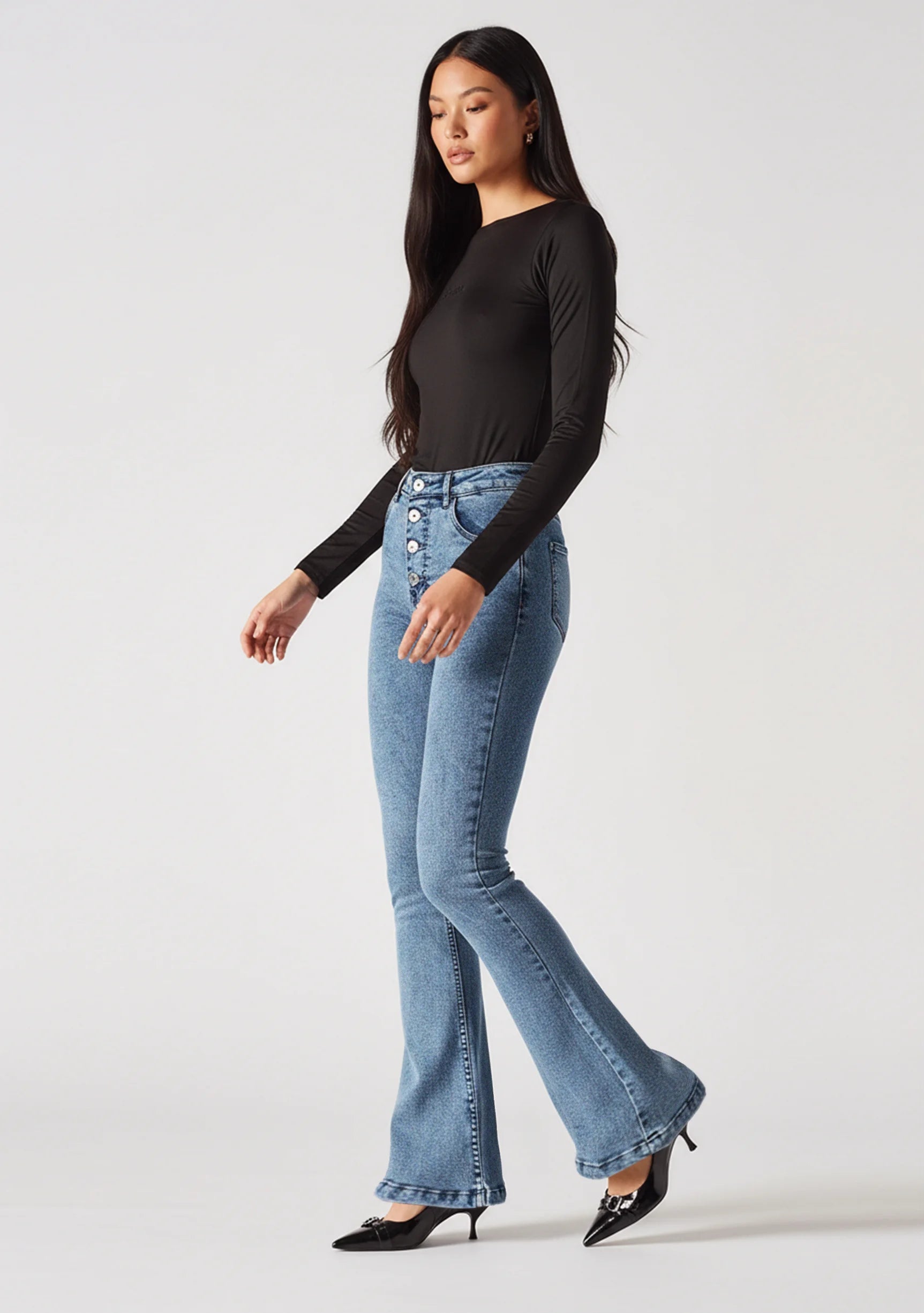 Front view of styled mid blue high-waisted bootcut jeans paired with a black top
