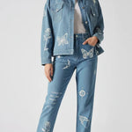 Full front standing pose of mid wash tattoo print denim jacket showing all embroidery details - women’s matching cargo pants with butterfly, rose, feather, and text motifs