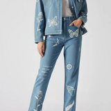 Full front standing pose of mid wash tattoo print denim jacket showing all embroidery details - women’s matching cargo pants with butterfly, rose, feather, and text motifs