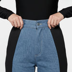 Close up of the waist fit and button closure on women's two-shade light blue and black jeans.