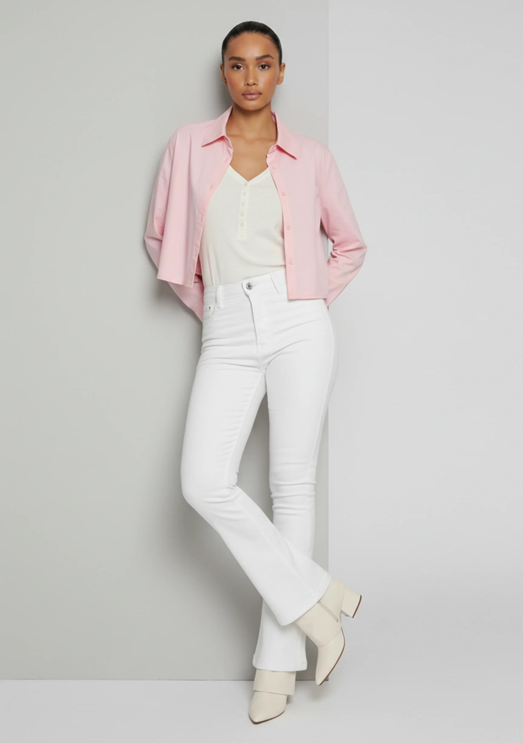 Model casually leaning against a wall wearing high-waisted white bootcut jeans