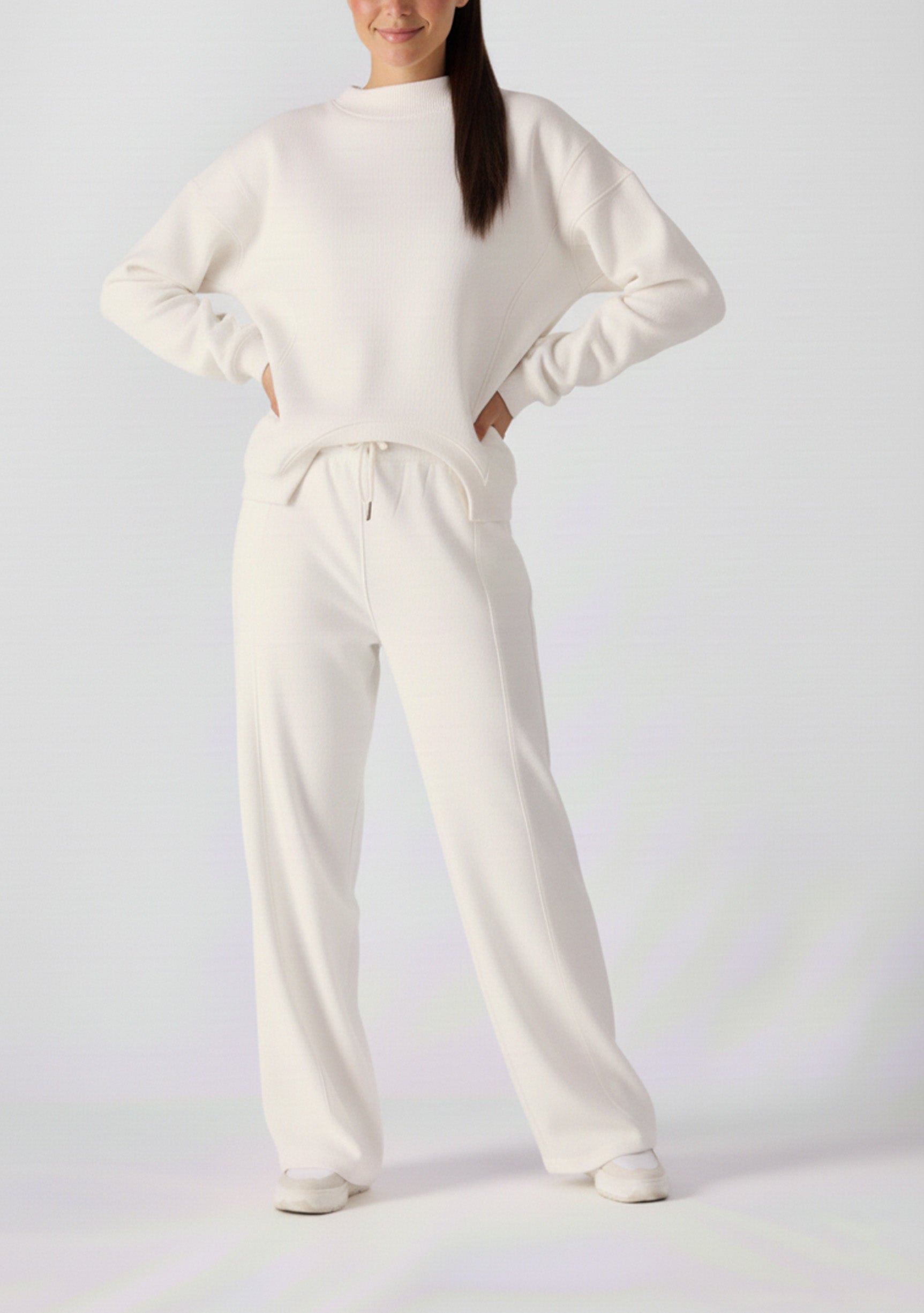 A woman posing with hands on hips wearing a white cotton jumper