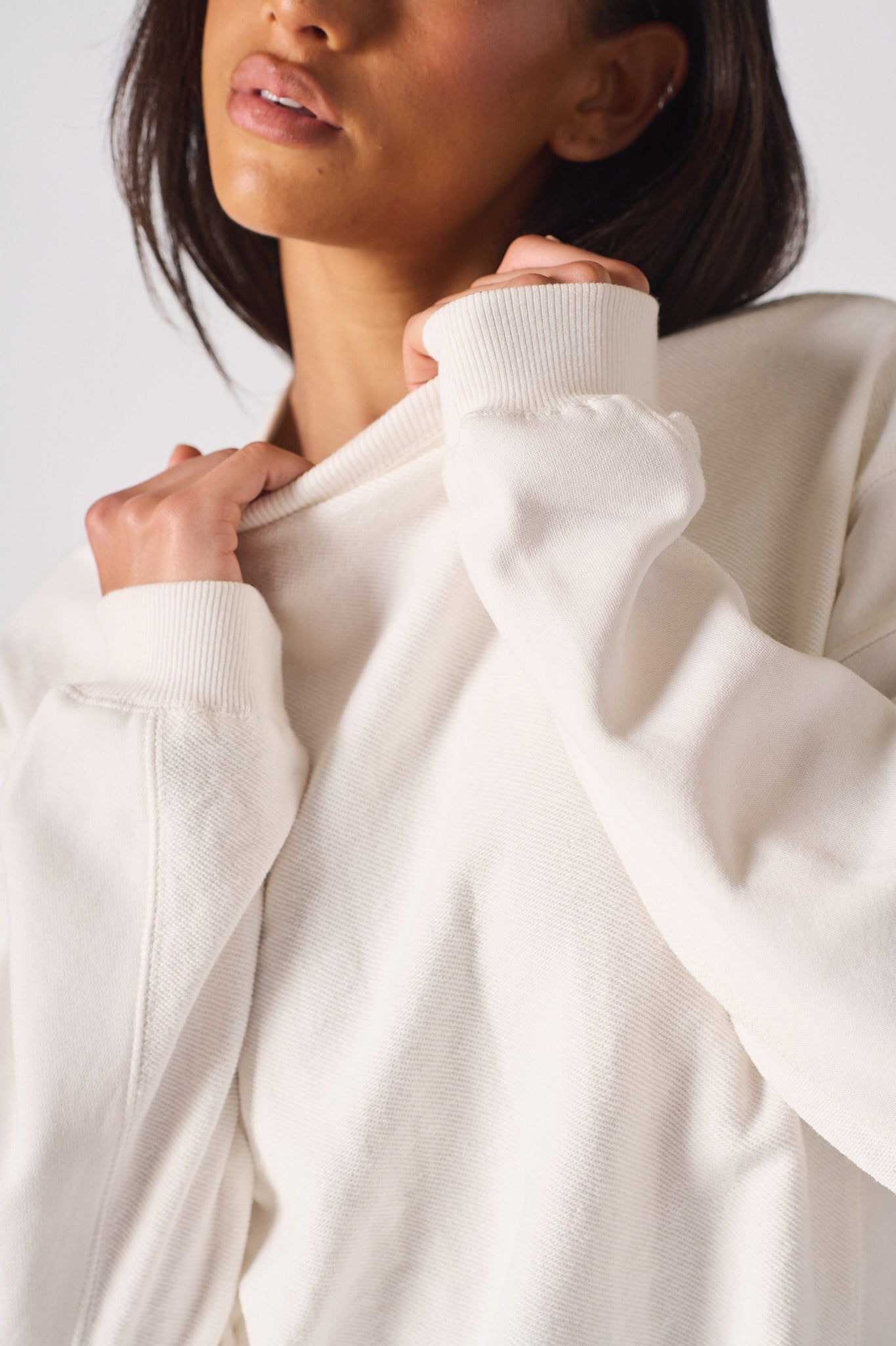 A woman adjusting the high neckline on a white cotton jumper