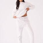 Full length view of a model in a white crew neck jumper pulling the hem for a stylish look