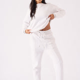 Full length view of a model in a white crew neck jumper pulling the hem for a stylish look