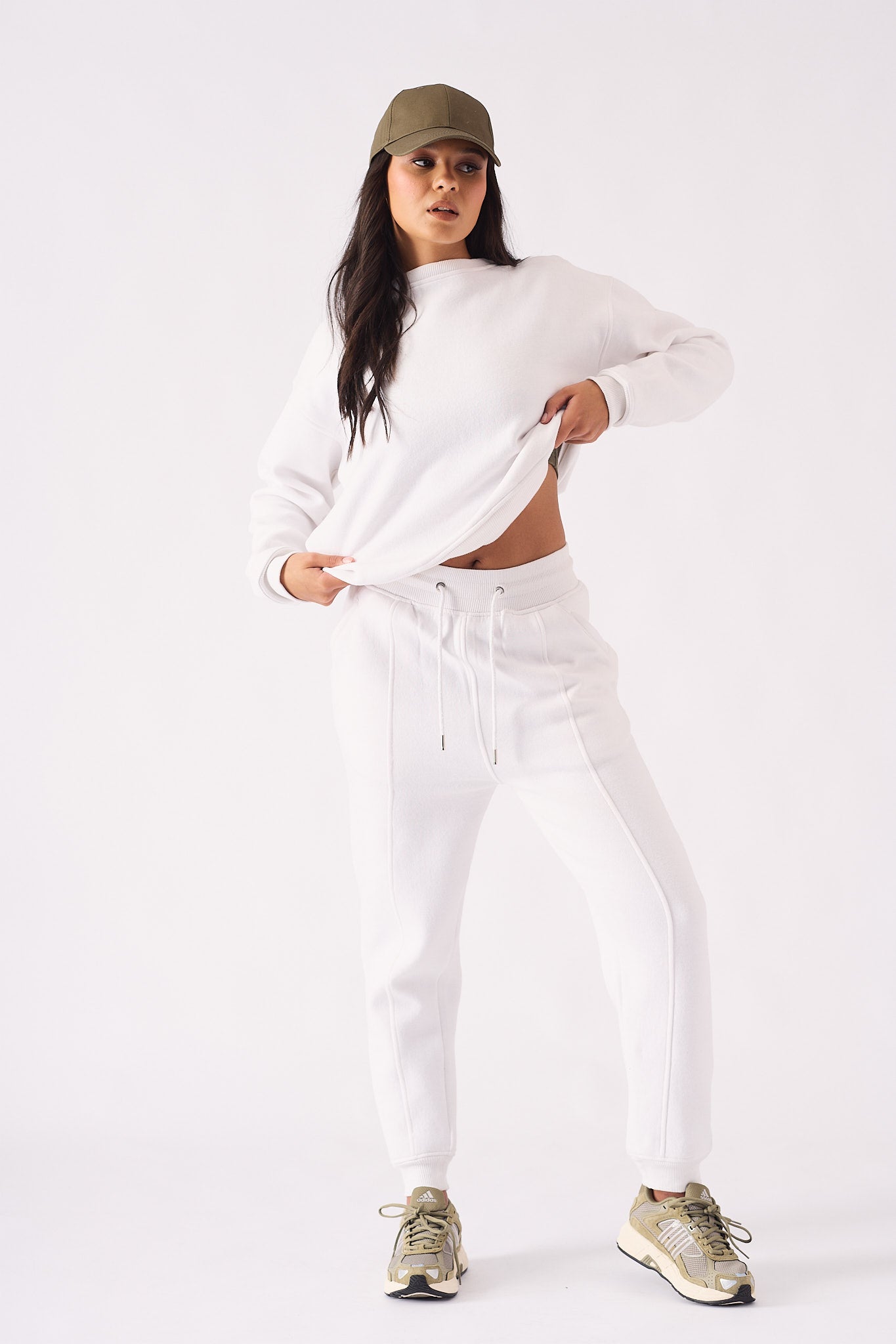 Full length view of a model in a white crew neck jumper pulling the hem for a stylish look